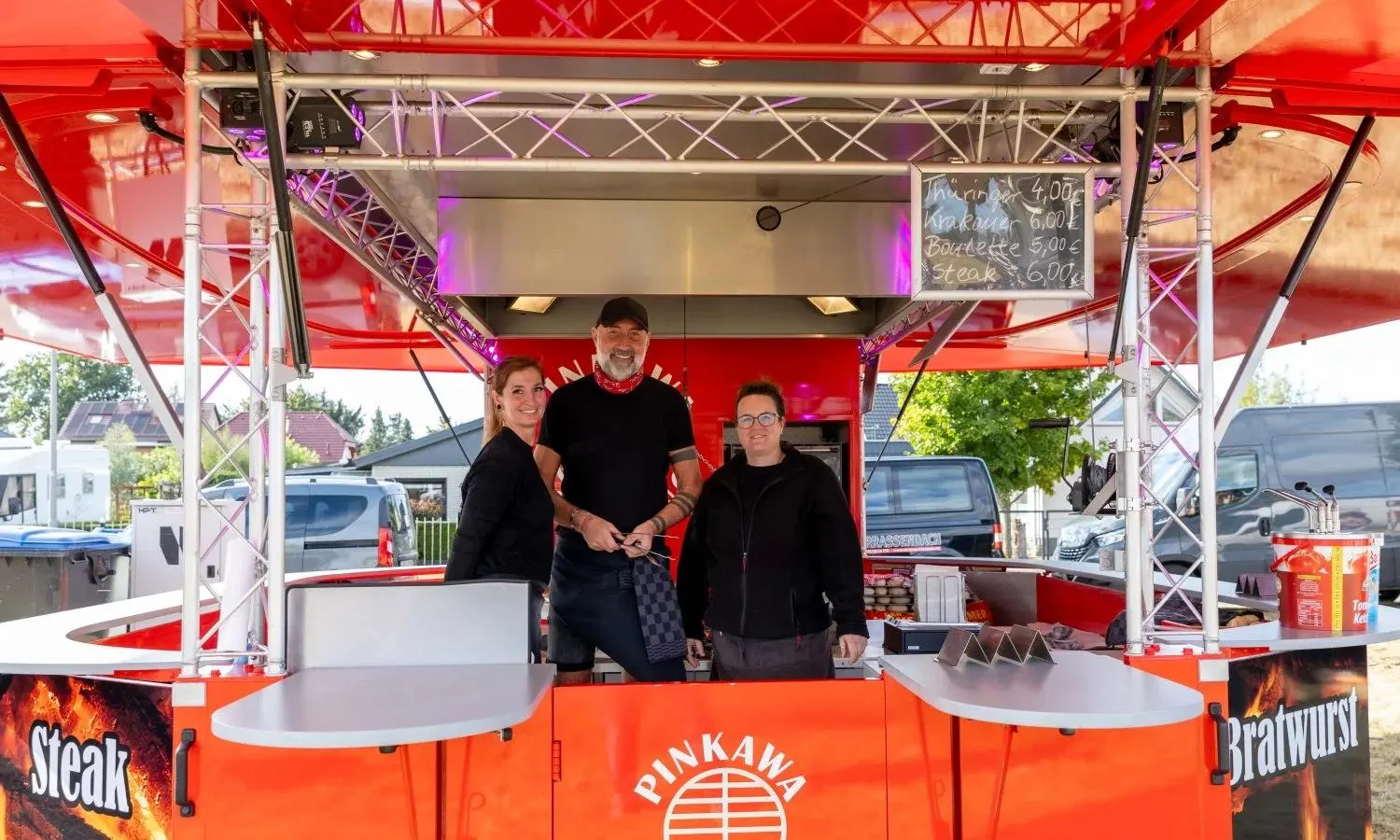 Drei Mitarbeitende im roten Grillwagen von Pinkawa Catering